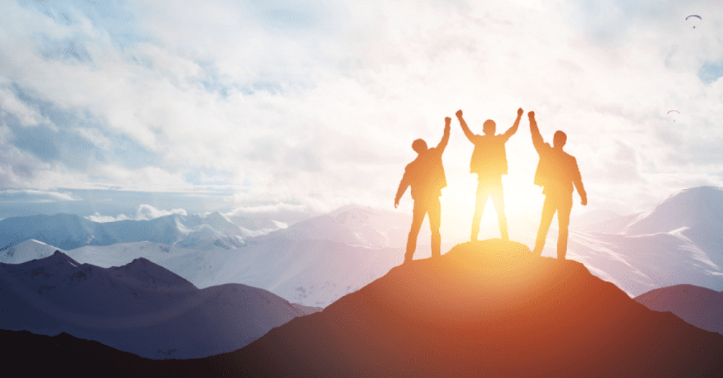 rês pessoas no topo de uma montanha, comemorando o sucesso ao nascer do sol.